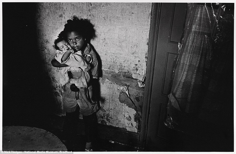 Простая Англия 1970-х Harrowing: A young girl tries to soothe a crying infant by holding it close to her chest. The pair stand in front of peeling, moulding wallpaper in what the photographer describes as a substandard property in Balsall Heath, Birmingham in June 1969