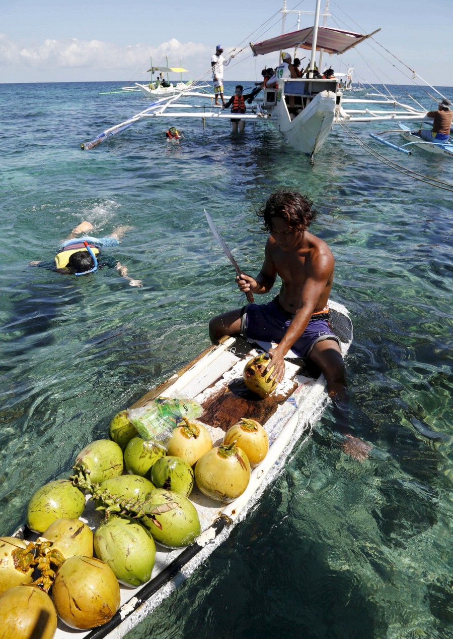 Подборка картинок 20.01.16 A vendor on his makeshift raft, chops a coconut to sell the juice to snorkelling tourists off the posh island of Boracay